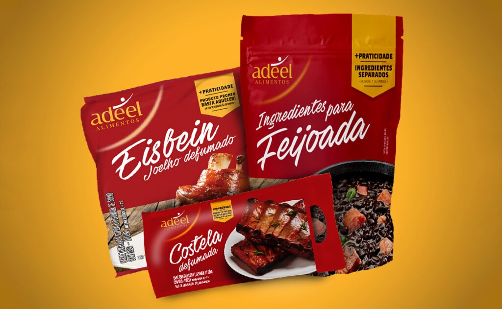 Três embalagens vermelhas da marca Adeel Alimentos para os produtos Eisbein Joelho defumado, Ingredientes para Feijoada e Costela defumada. As embalagens apresentam letras cursivas brancas, selos amarelos de praticidade e fotos realistas dos pratos prontos na parte inferior.